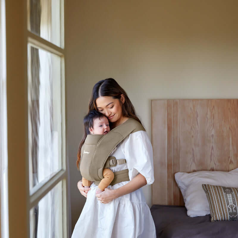 Mom carrying baby in Ergobaby Embrace - Soft Olive carrier, showcasing comfort and ergonomic design | Babymaxi