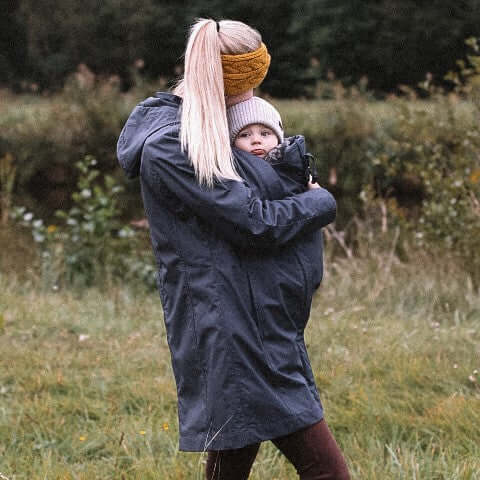 Woman wearing Mamalila Berlin All Season Babywearing Coat – Navy while carrying a child outdoors | Babymaxi