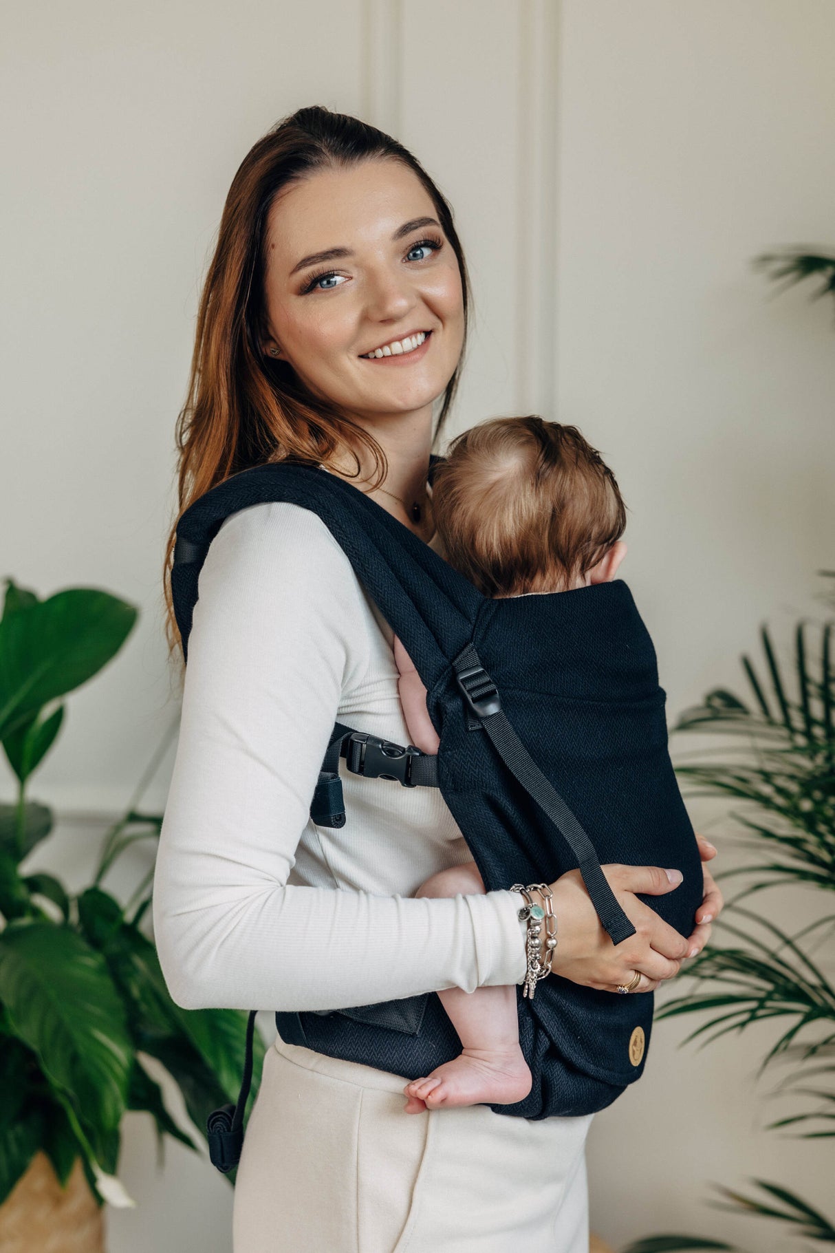 Smiling woman holding a baby in a black cotton baby carrier, LennyLight, showcasing comfort and versatility.