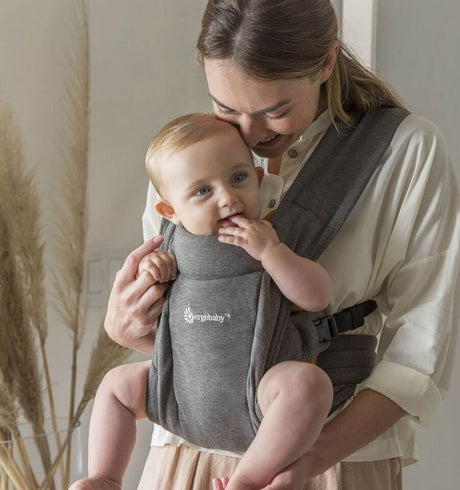 Mom holding baby in Ergobaby Embrace - Heather Grey carrier, showcasing comfort and style | Babymaxi