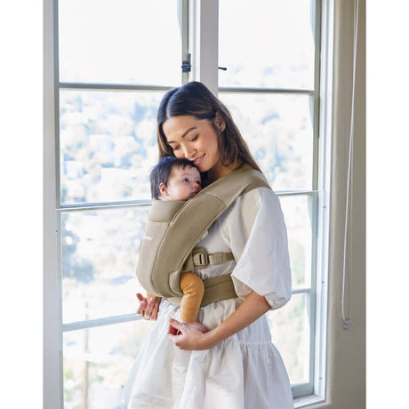 Ergobaby Embrace - Soft Olive baby carrier being used by a mother with her baby, showcasing comfort and ergonomic design | Babymaxi