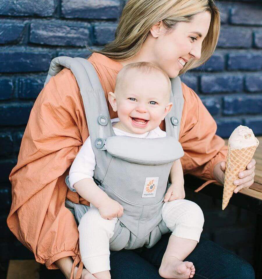 Mother smiling with baby in Ergobaby Omni Classic Cotton Carrier - Pearl Grey, enjoying ice cream outdoors | Babymaxi