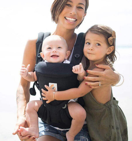 Mother using Ergobaby Omni Classic Cotton Carrier - Pure Black with baby, smiling toddler beside her | Babymaxi