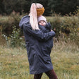 Woman wearing Mamalila Berlin All Season Babywearing Coat – Navy while carrying a child outdoors | Babymaxi