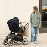 Mamalila Boston Babywearing Jacket - Agave worn by a woman next to a stroller, perfect for mother and baby on-the-go | Babymaxi