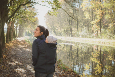 Woman wearing Mamalila Softshell Babywearing Jacket Allrounder - Navy while walking with a baby in a scenic autumn setting | Babymaxi