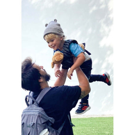 Joyful child with teddy bear in Manduca Doll Carrier - Zebra, enjoying playful moments with dad | Babymaxi