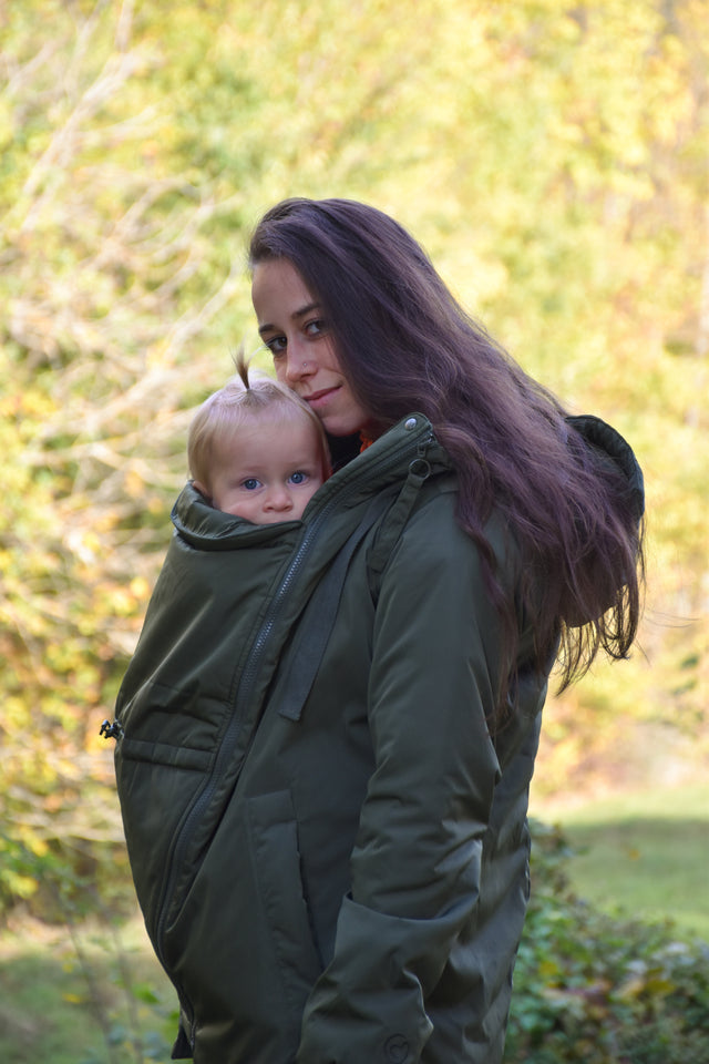 Mamalila Boston Babywearing Jacket Olive, mother carrying baby on front in green babywearing coat outdoors