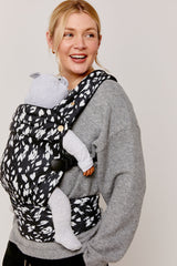 Woman wearing a baby in a carrier with a black and white pattern on a plain background